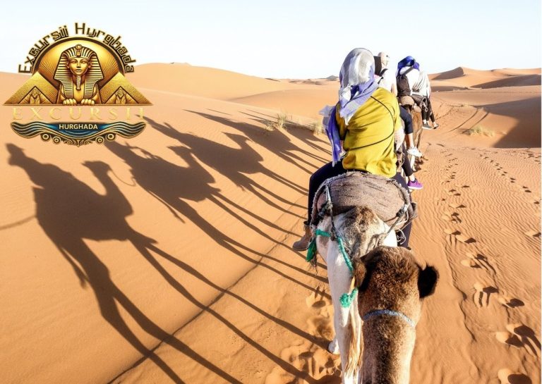 Turiști călărind cămile într-o Excursie Safari în Hurghada la apus, formând umbre lungi pe dunele de nisip ale deșertului.